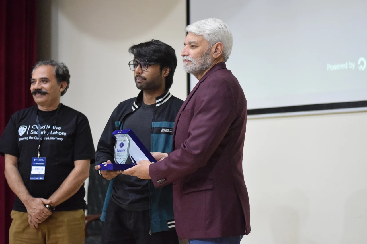 Mahad and a presenter hold an open Hacktoberfest award case on stage.